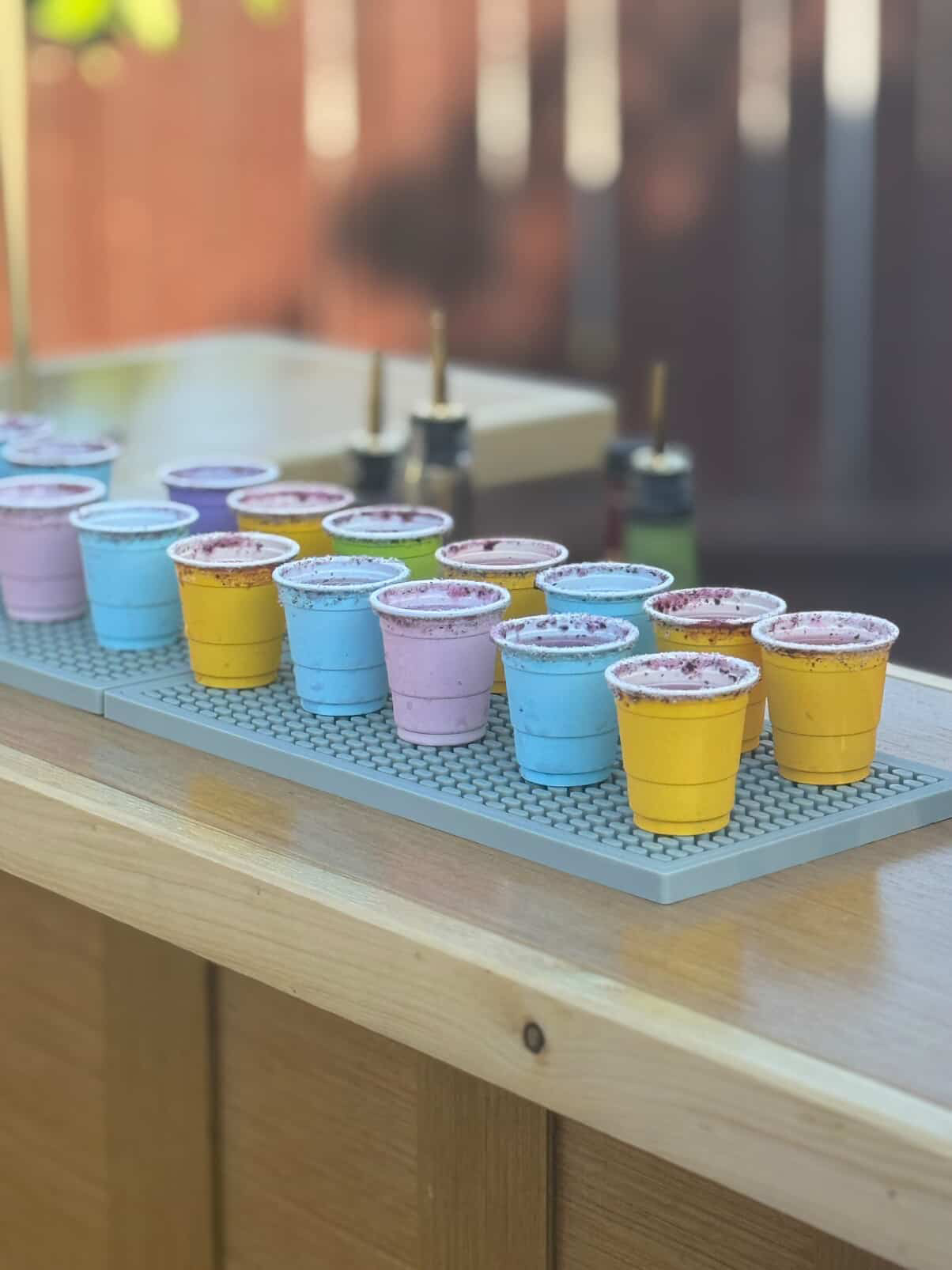 Colorful shot glasses with sugar rims lined up on the bar mat