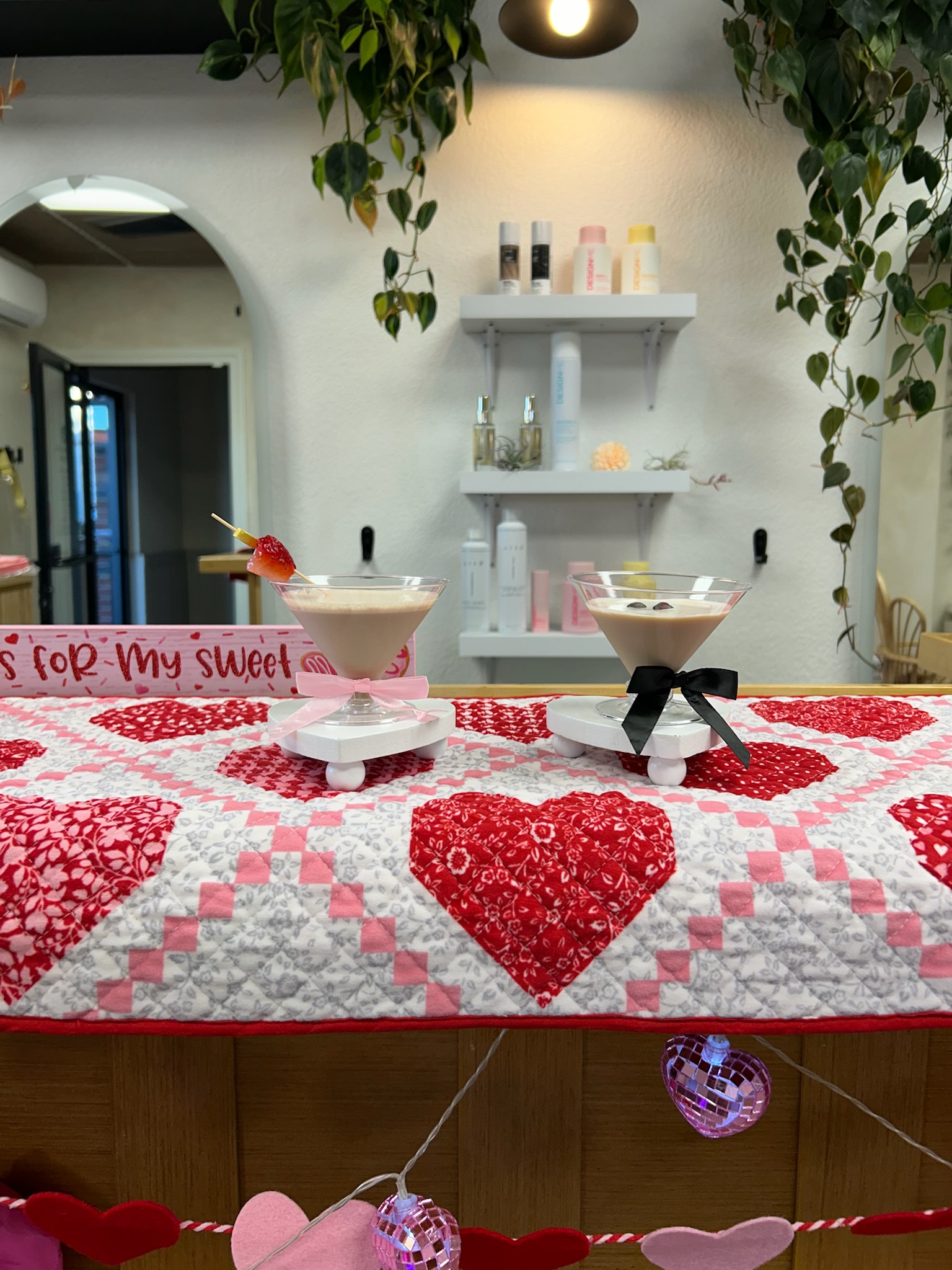 Two chocolate martinis in coupe glasses set on a Valentine's Day heart-pattern quilt runner inside a boutique salon