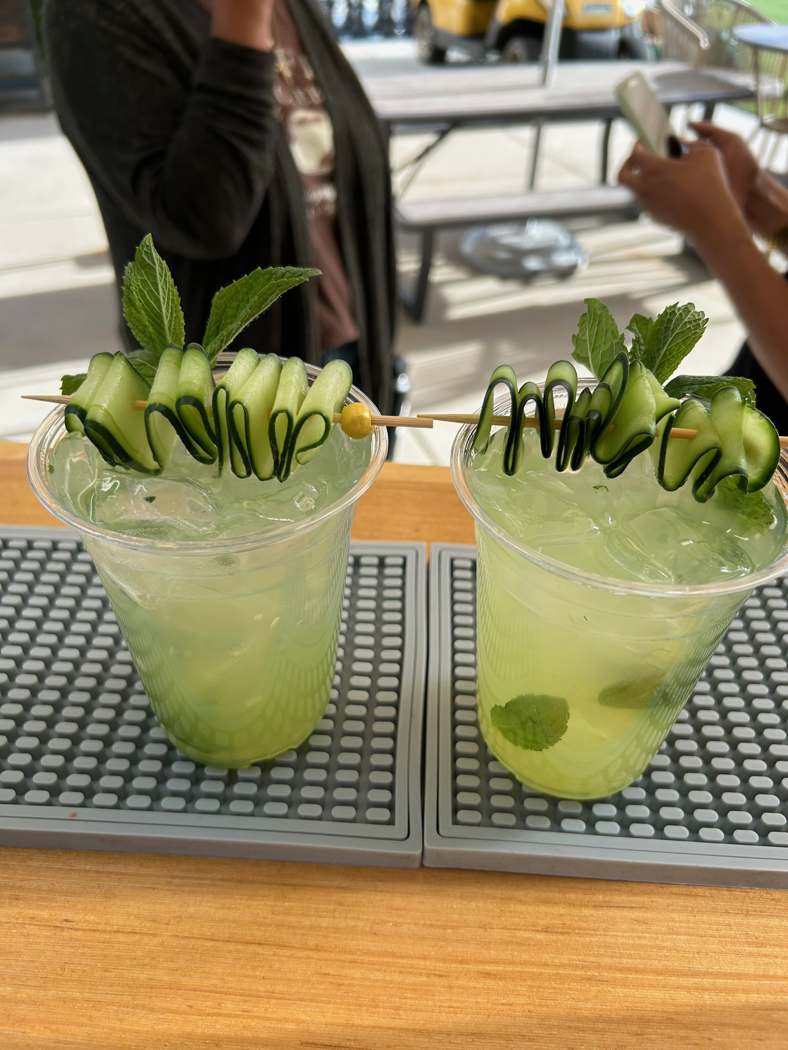 Two cucumber mint cocktails with spiraled cucumber ribbon garnishes on the bar