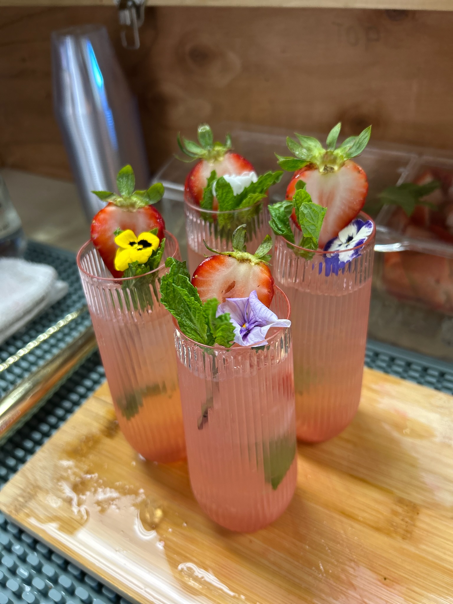 Three pink strawberry mocktails garnished with fresh strawberries, mint, and edible pansies in ribbed glasses