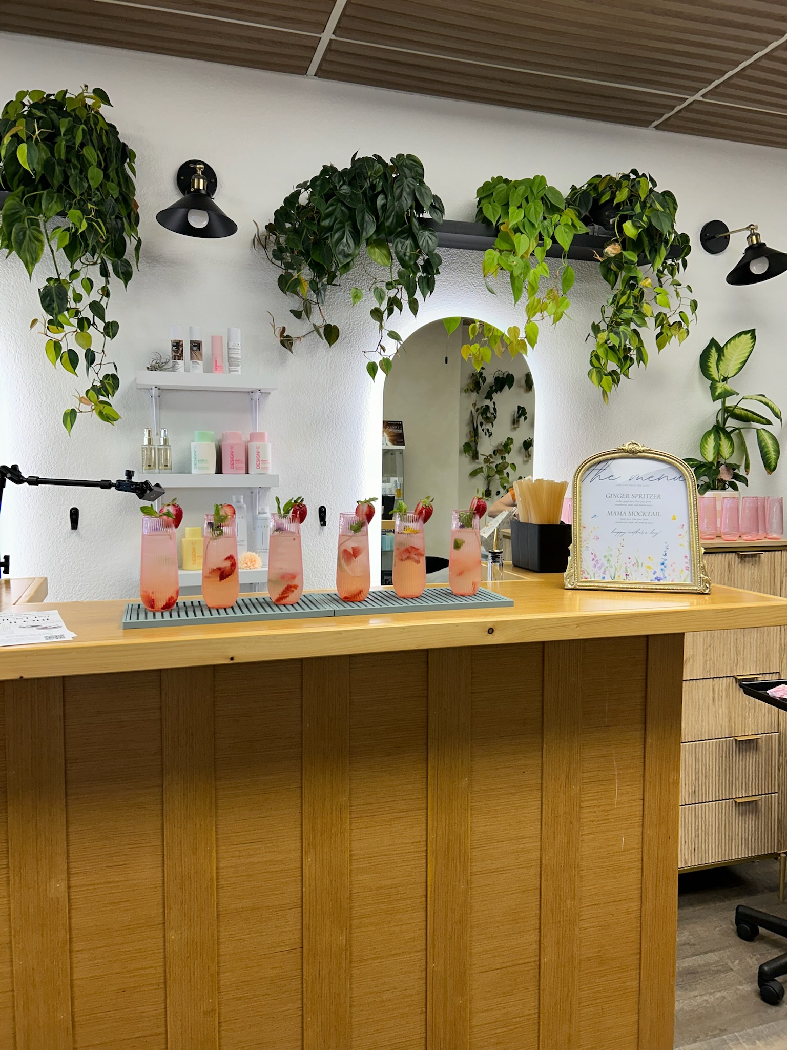 Pink strawberry cocktails lined up on a styled bar inside a beautifully decorated venue with trailing greenery