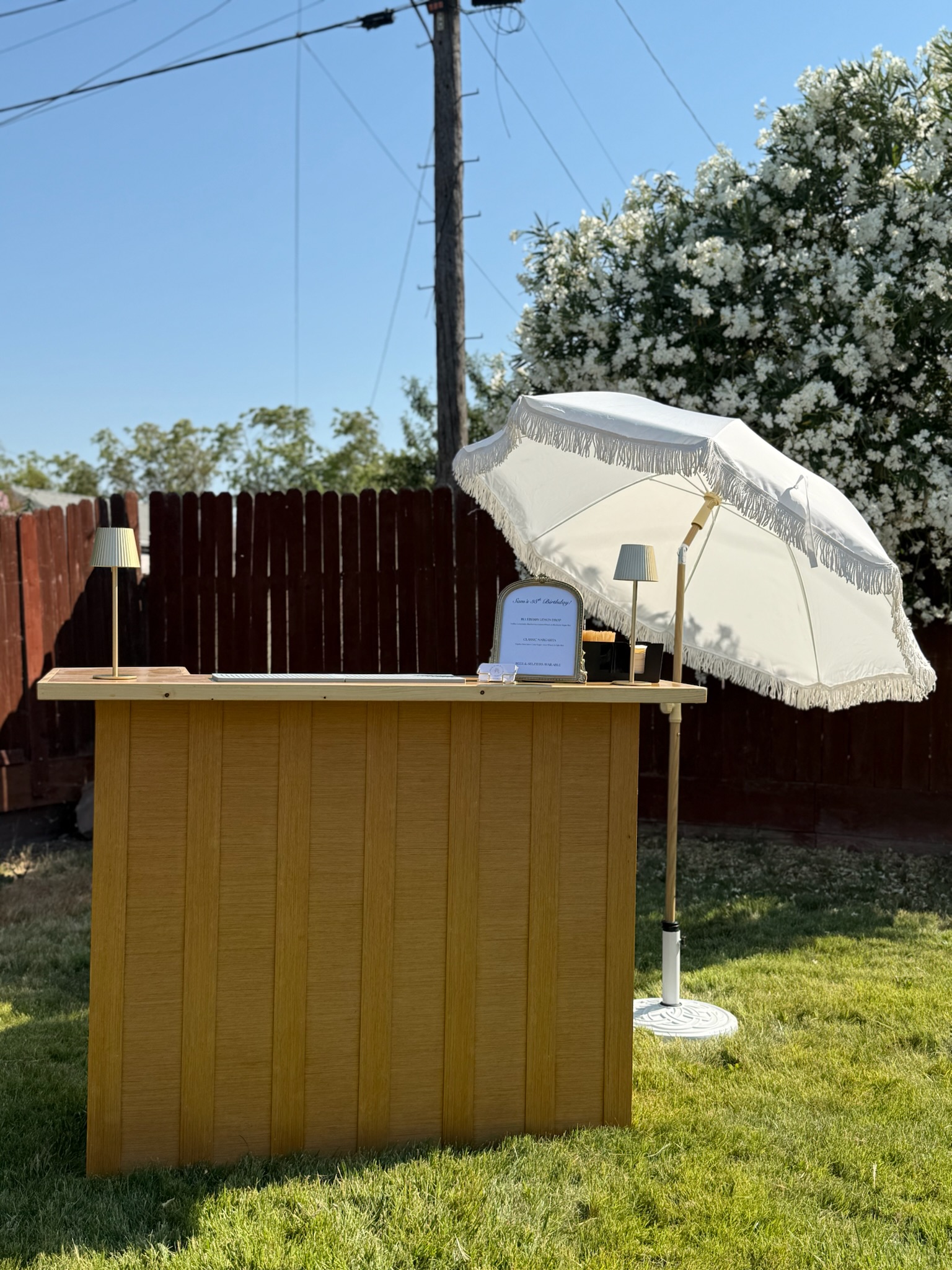 Pour It Out mobile bar set up in a sunny backyard under a white flowering tree, ready for service