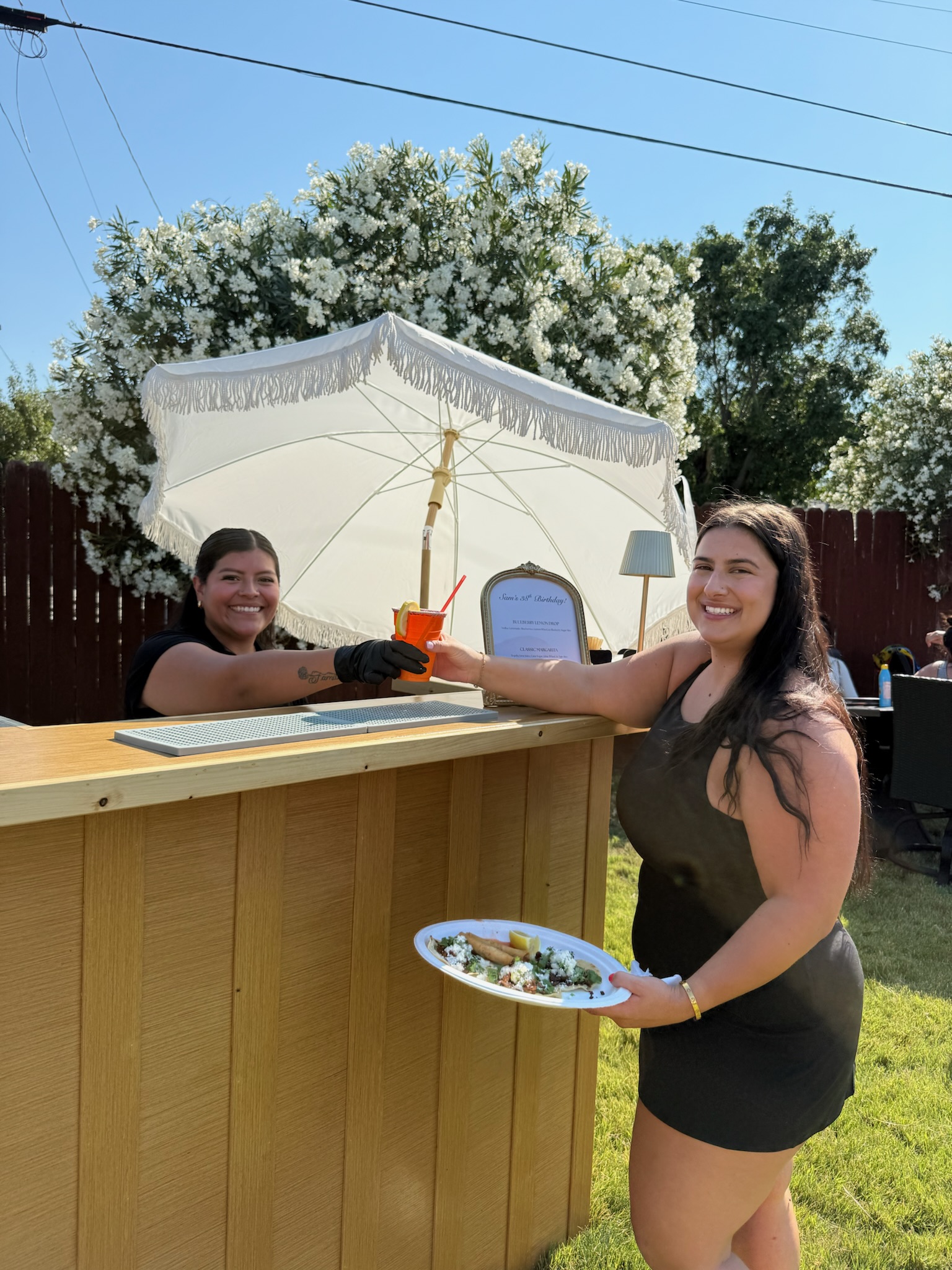 Pour It Out bartender smiling as she hands a drink to a happy guest at a sunny backyard party