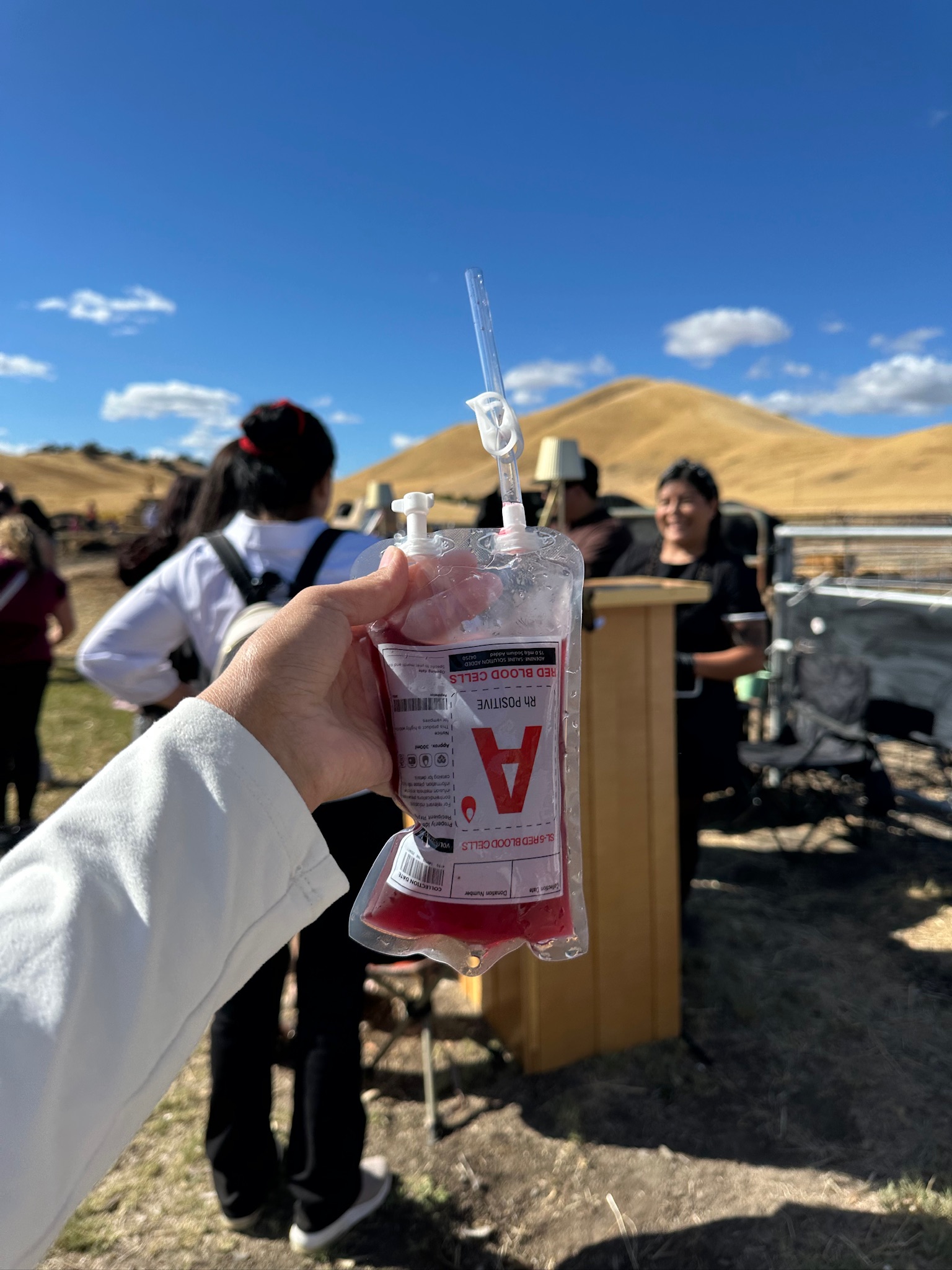 Guest holding a spooky Halloween blood bag cocktail at an outdoor equestrian event in the rolling hills