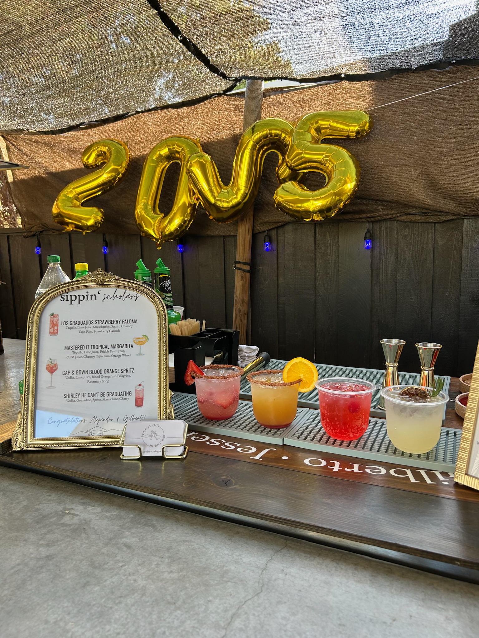 Graduation party bar setup with a full cocktail lineup and gold 2025 number balloons overhead