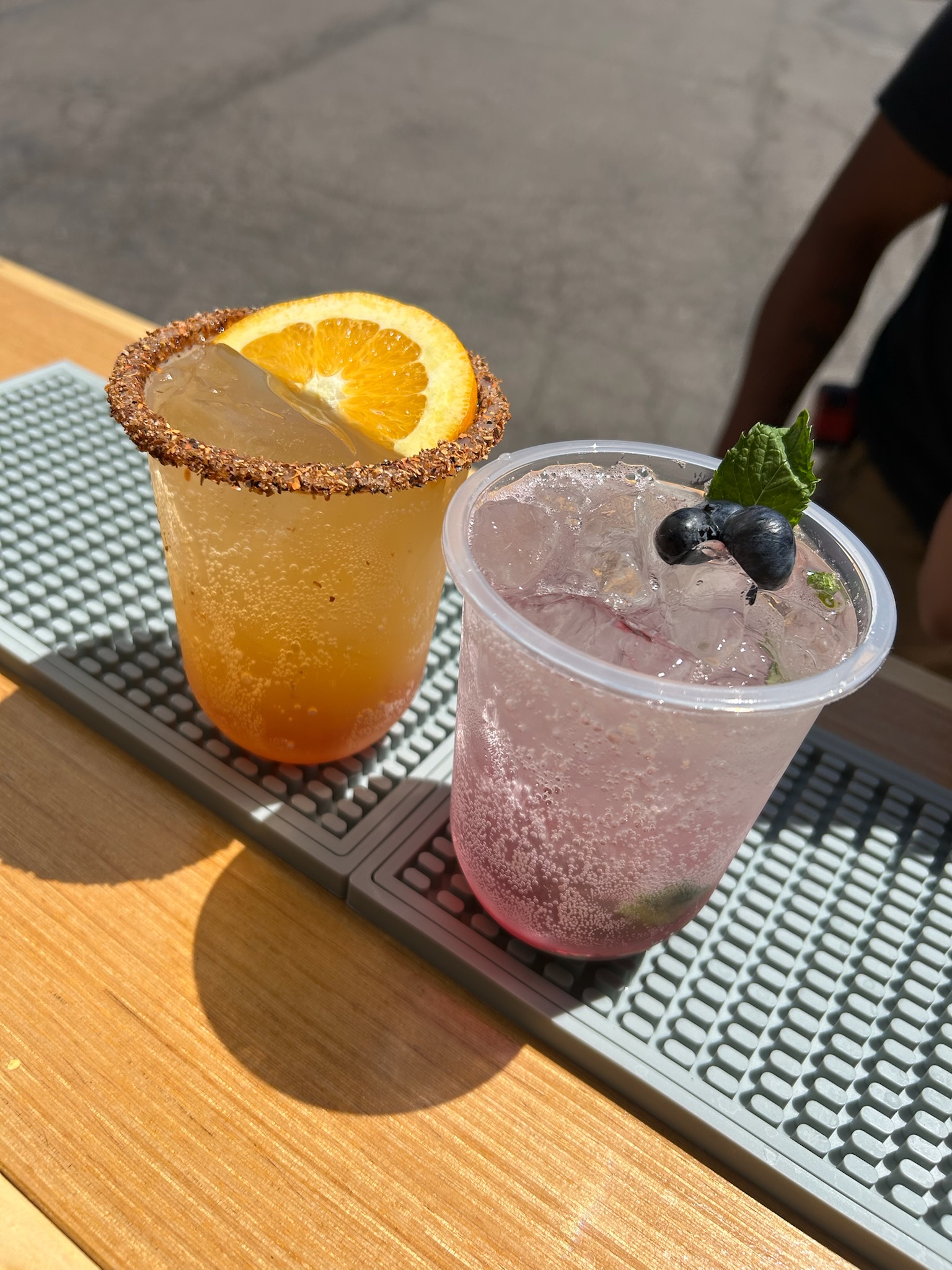 Two cocktails side by side: a tajin-rimmed orange Paloma and a sparkling blueberry mint drink