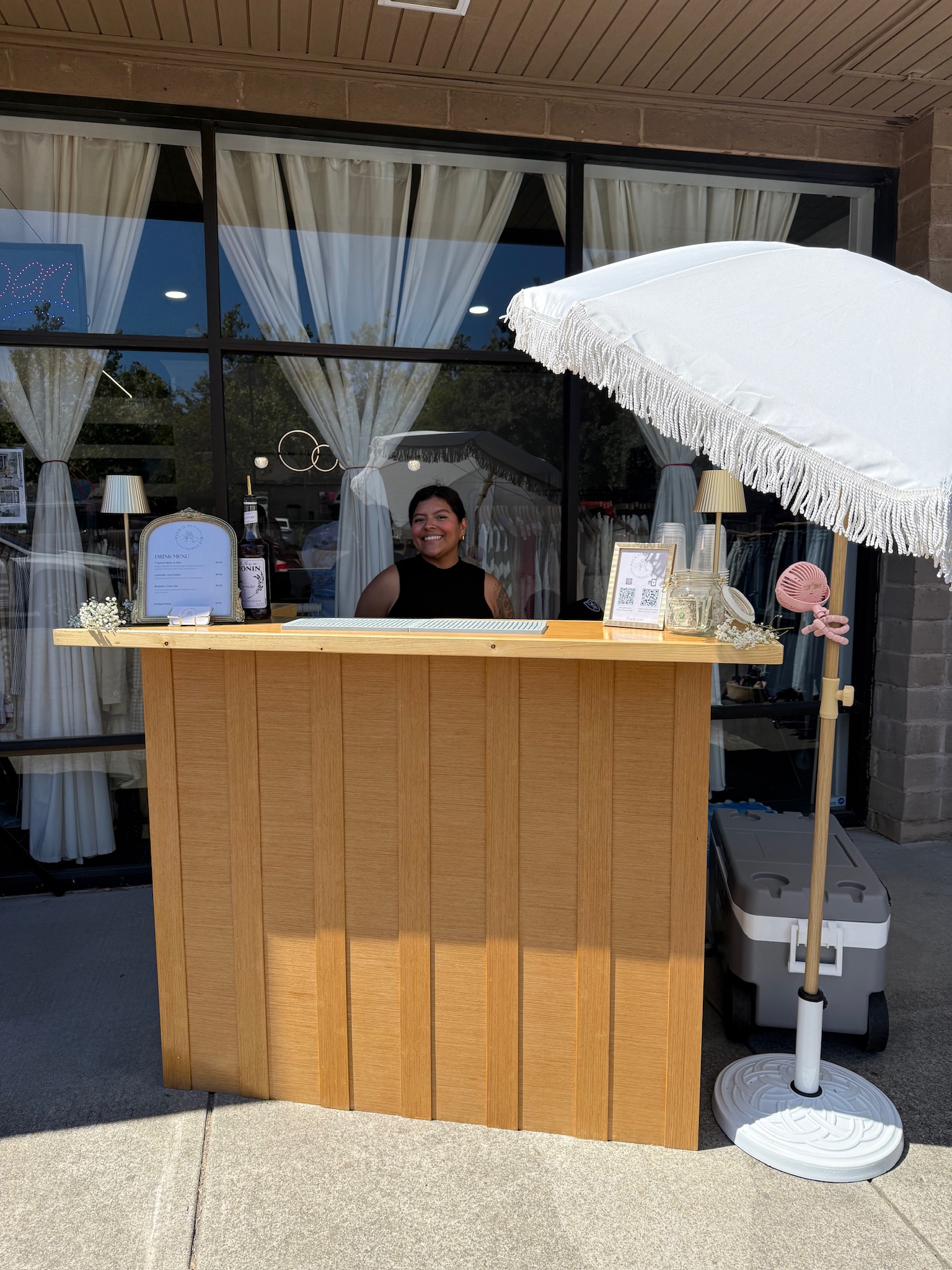 Owner smiling behind the Pour It Out mobile bar set up in front of a boutique storefront