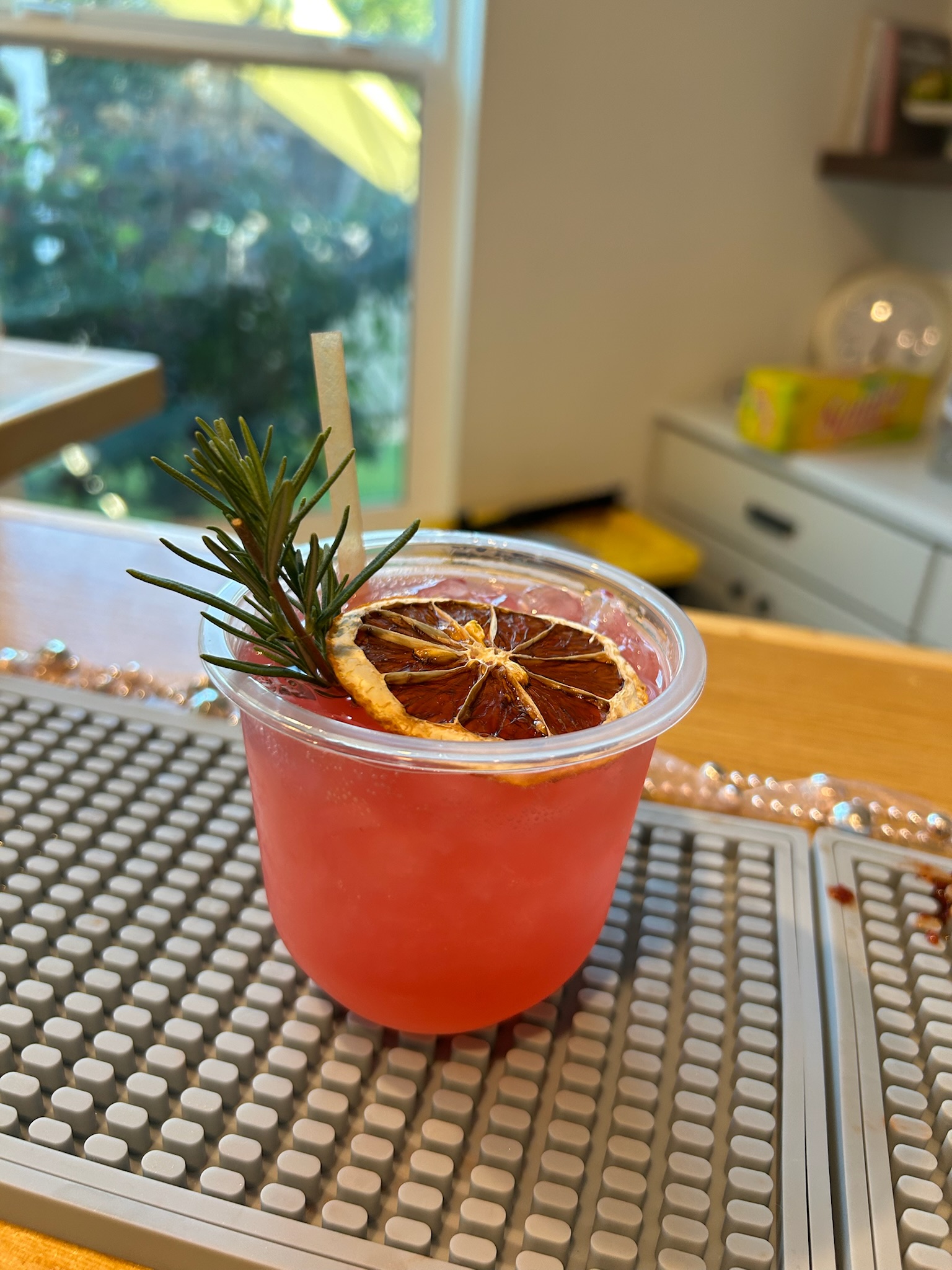 Pink cocktail garnished with a dried blood orange wheel and fresh rosemary sprig