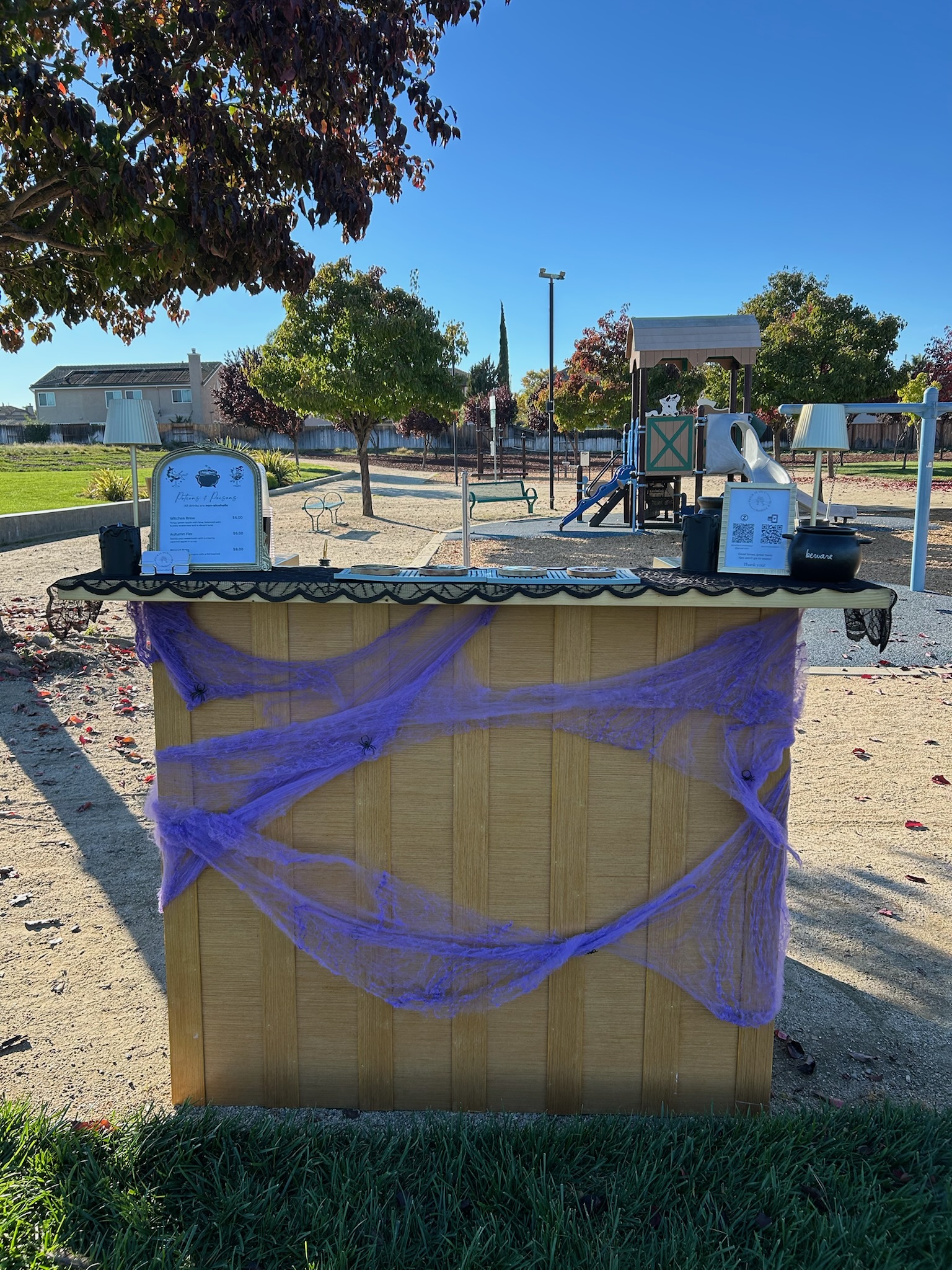 Mobile bar decorated with purple cobwebs and Halloween decor set up outdoors at a park