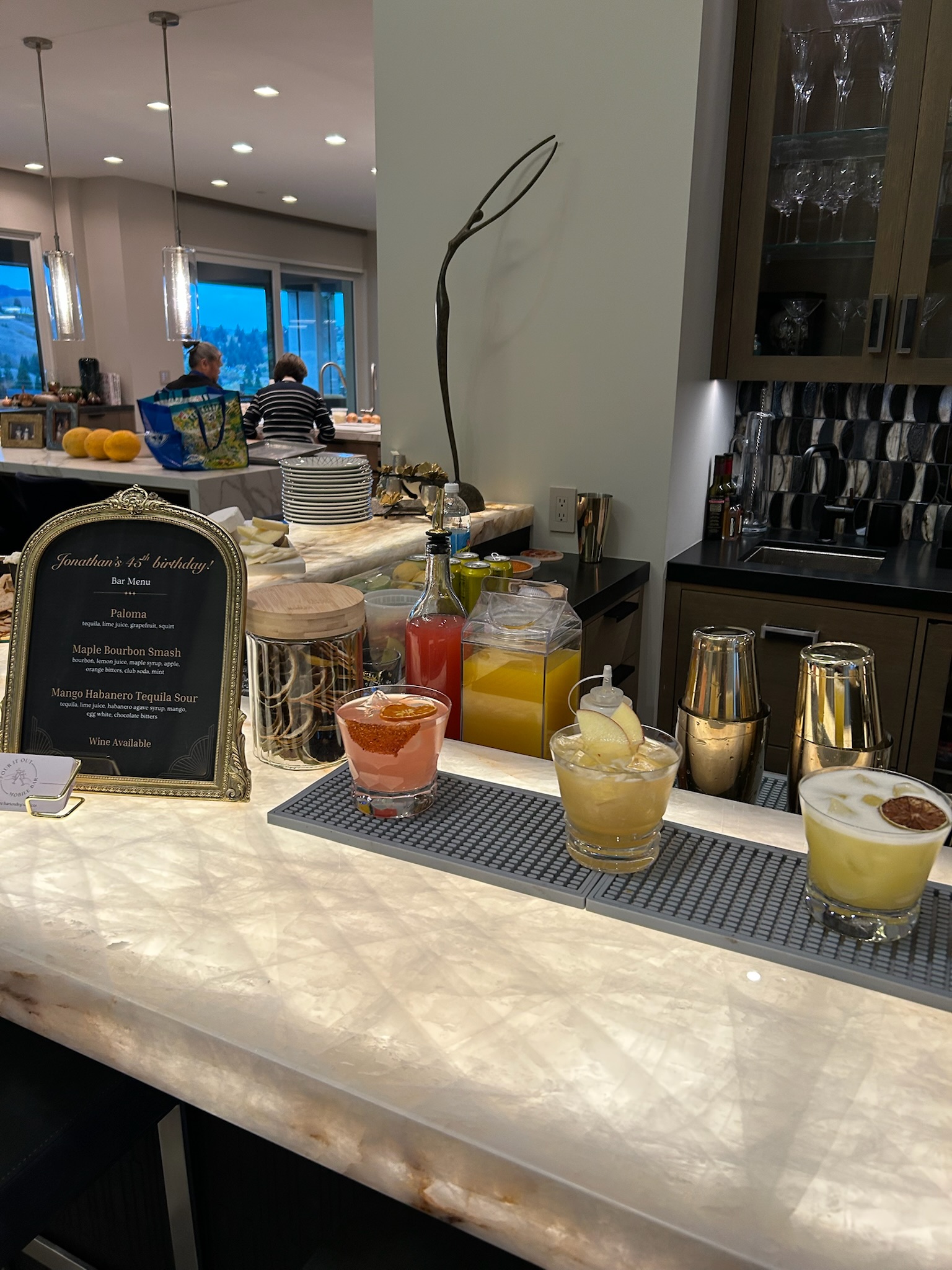 Three cocktails on an elegant marble bar top at a birthday party: a Paloma, a Maple Bourbon Smash, and a Mango Habanero Tequila Sour