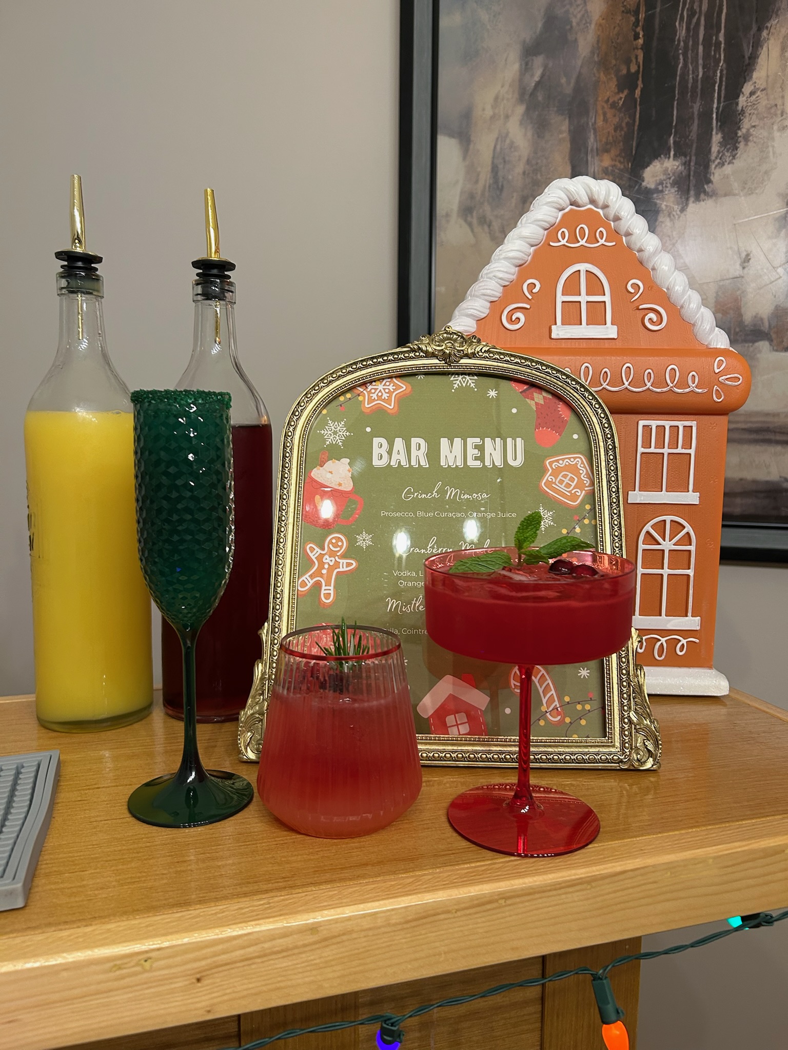 Christmas holiday cocktails: a sparkling cranberry margarita in a red coupe and a festive green champagne flute beside a gingerbread-themed bar menu